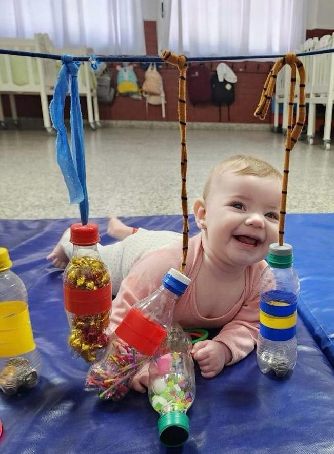 Bebé sonríe durante una actividad de estimulación temprana con materiales sensoriales en sala maternal.
